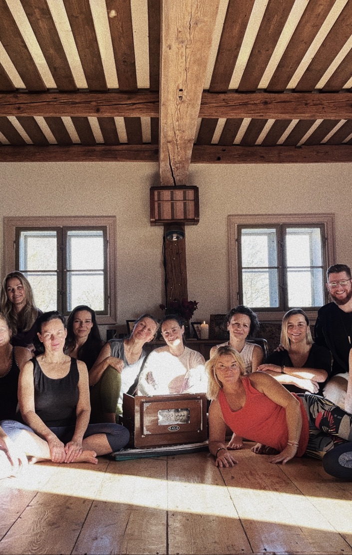 Účastníci jógového retreatu sedí společně v dřevěné světnici s harmoniem